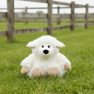 Plush lamb toy on grass with wooden fence in the background