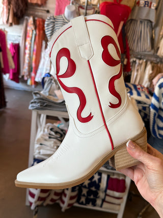 White cowboy boot with red bow designs held in a store setting