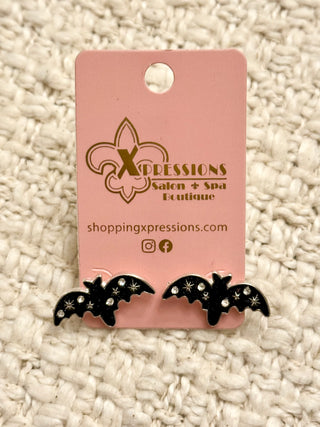 Black bat-shaped earrings on a pink 'Xpressions Salon & Spa Boutique' card against a textured beige background.