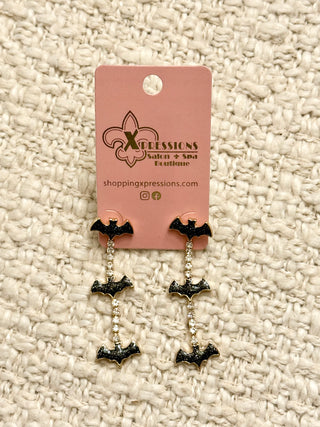 Bat-shaped earrings on a pink Xpressions card against a textured beige background