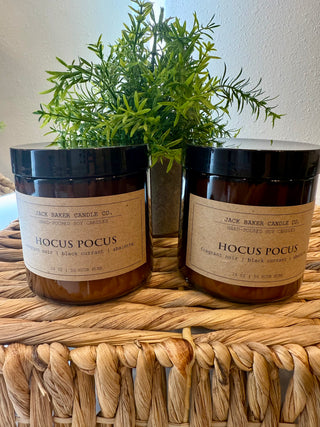 Two 'Hocus Pocus' candles from Jack Baker Candle Co. on a woven surface with a plant in the background.