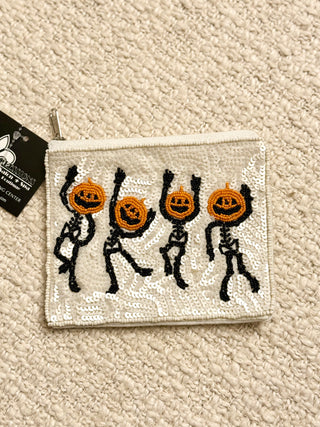 Halloween-themed sequin pouch with skeletons and pumpkins on a beige carpet