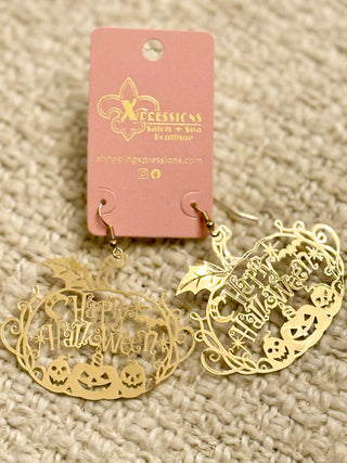 Gold Halloween-themed earrings on a textured beige surface with a pink card displaying 'Xpressions' branding.