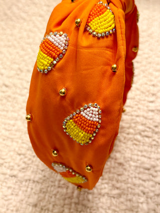 Orange fabric headband with candy corn patterns and gold beads on a beige background
