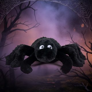 Plush spider toy against a Halloween-themed background with spider webs and a dark sky.