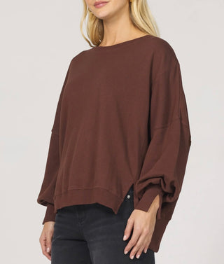Woman wearing a long sleeve brown top with slits on cuffs around the wrist