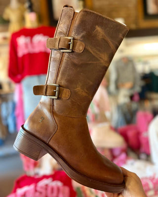 Brown leather boot with buckles held in front of a store background