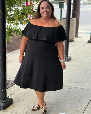 Woman wearing a black off-shoulder dress on a sidewalk.