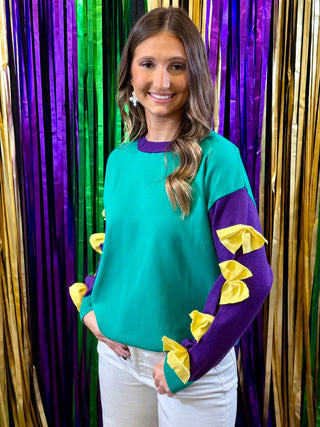 Woman wearing a teal sweater with purple and yellow accents in front of colorful streamers.
