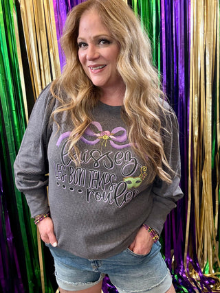 Woman wearing a gray long sleeve shirt with a colorful design in front of a multicolored curtain.