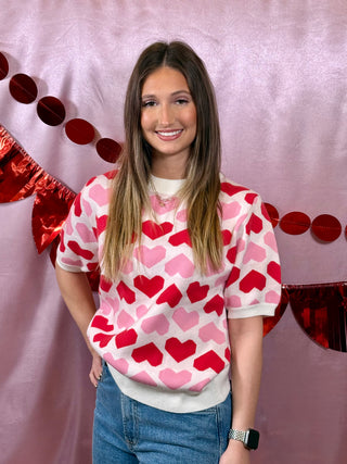 Person wearing a heart-patterned sweater with a pink background