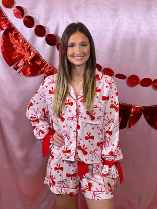 Woman wearing a white pajama set with red bows against a decorative red heart background