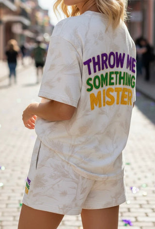 Woman standing in street wearing camo set with shirt and shorts that say “Throw Me Something Mister”