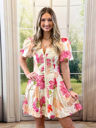 Woman wearing a floral dress standing in front of a window with a view of greenery.