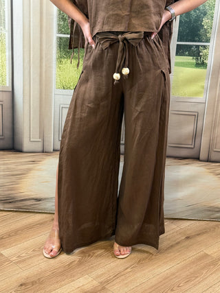 Person wearing a brown outfit with wide-leg pants in a room with large windows.