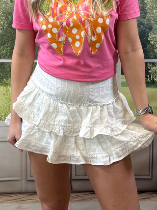 Person wearing a pink shirt with a colorful butterfly design and a white ruffled skirt.