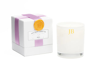 White candle with 'JB' branding next to its packaging box on a white background