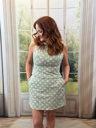Woman wearing a light green set with a floral pattern in a room with large windows.