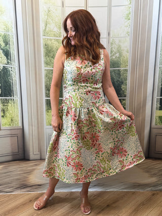 Woman in a floral dress standing in a room with large windows.