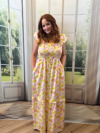 Woman wearing a floral dress standing in a room with large windows.