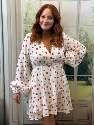 Woman wearing a white dress with red strawberries front of a glass door.