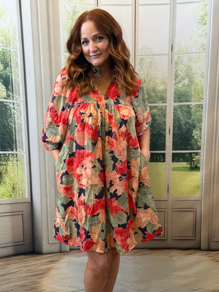 Woman wearing a floral dress standing in front of large windows with a garden view.
