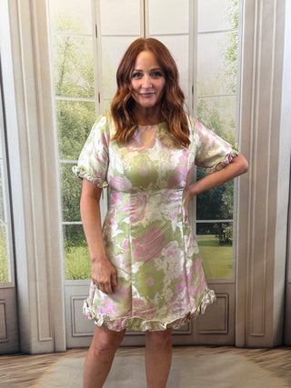 Woman wearing a floral dress standing in front of a window with curtains.