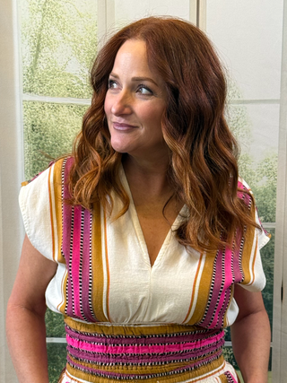 Woman wearing a colorful striped top in a room with a window in the background