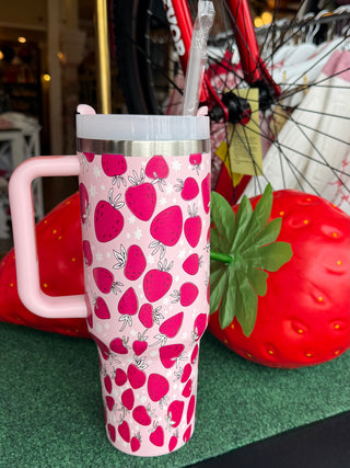 Travel mug with strawberry pattern and pink handle, surrounded by strawberry decorations.